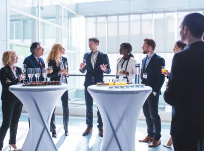 Business coworkers standing in a lobby. They are looking at each other and holding glasses of champagne and juice.